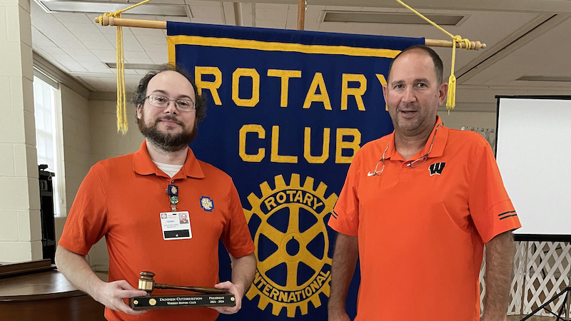 Two men standing in front of a rotary club banner.
