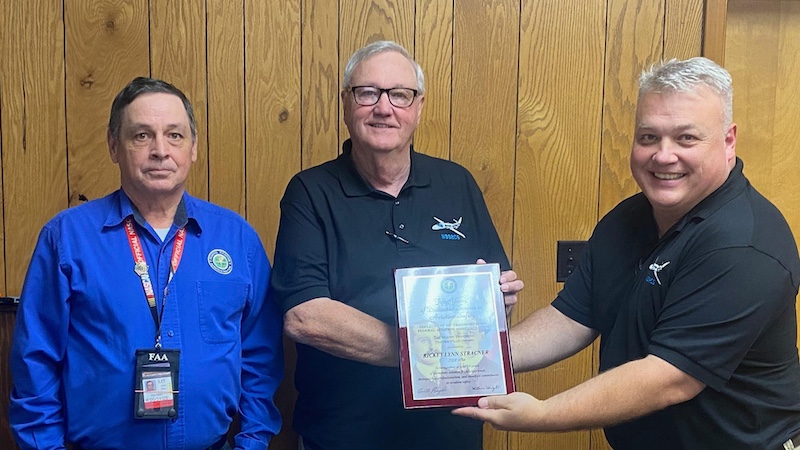 A man holding a plaque in front of two other men.