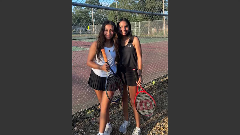 Two girls posing for a picture with tennis rackets.
