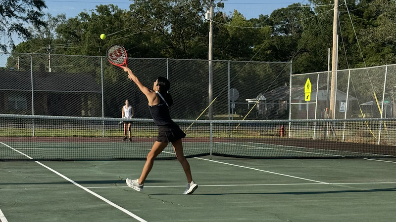 A woman swinging at a tennis ball with her racket.
