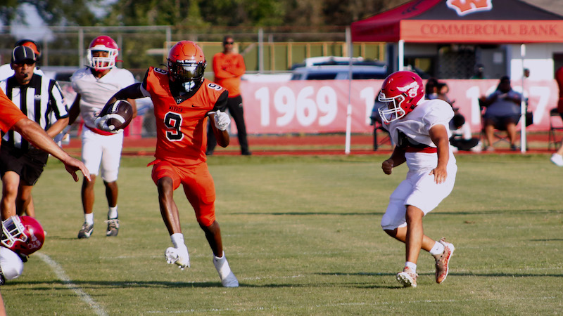 A football player running with the ball while another player is in position to catch it.