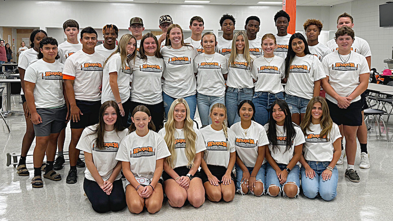 A group of people wearing white shirts and sitting on the ground.