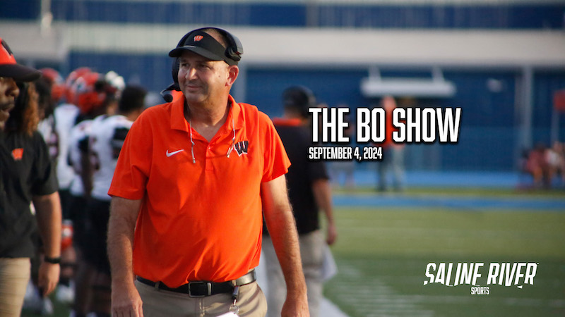 A man in an orange shirt is standing on the field.
