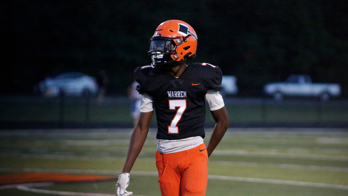 A football player in an orange uniform is walking on the field.