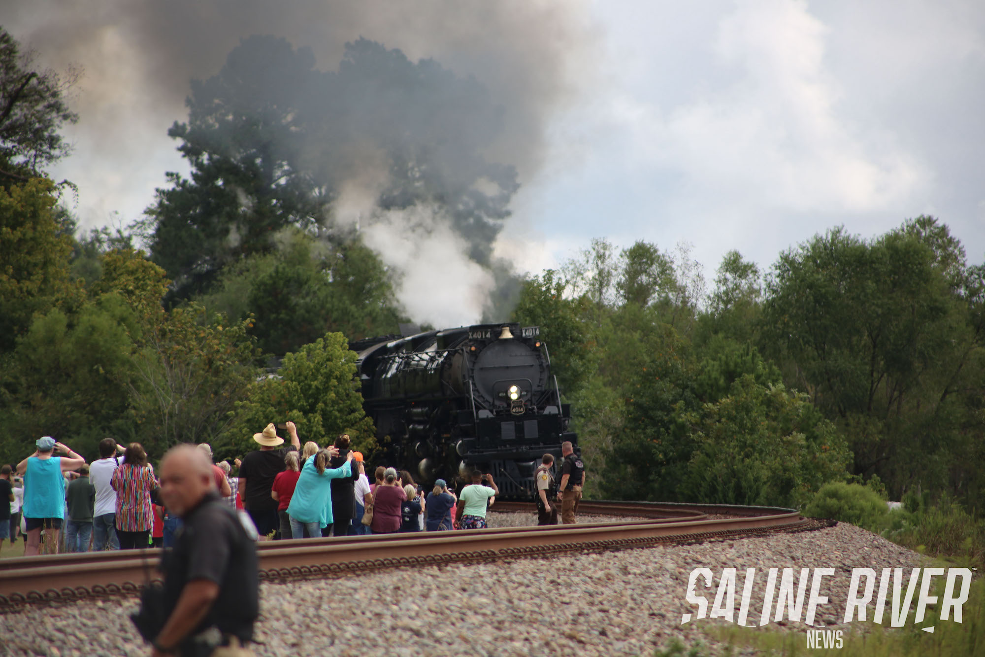 A train traveling down tracks near trees and people.