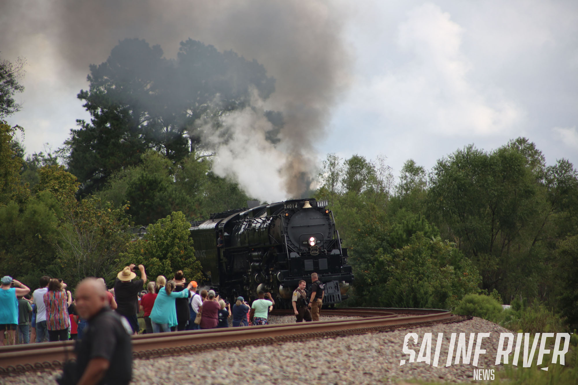 A train traveling down tracks near trees and people.