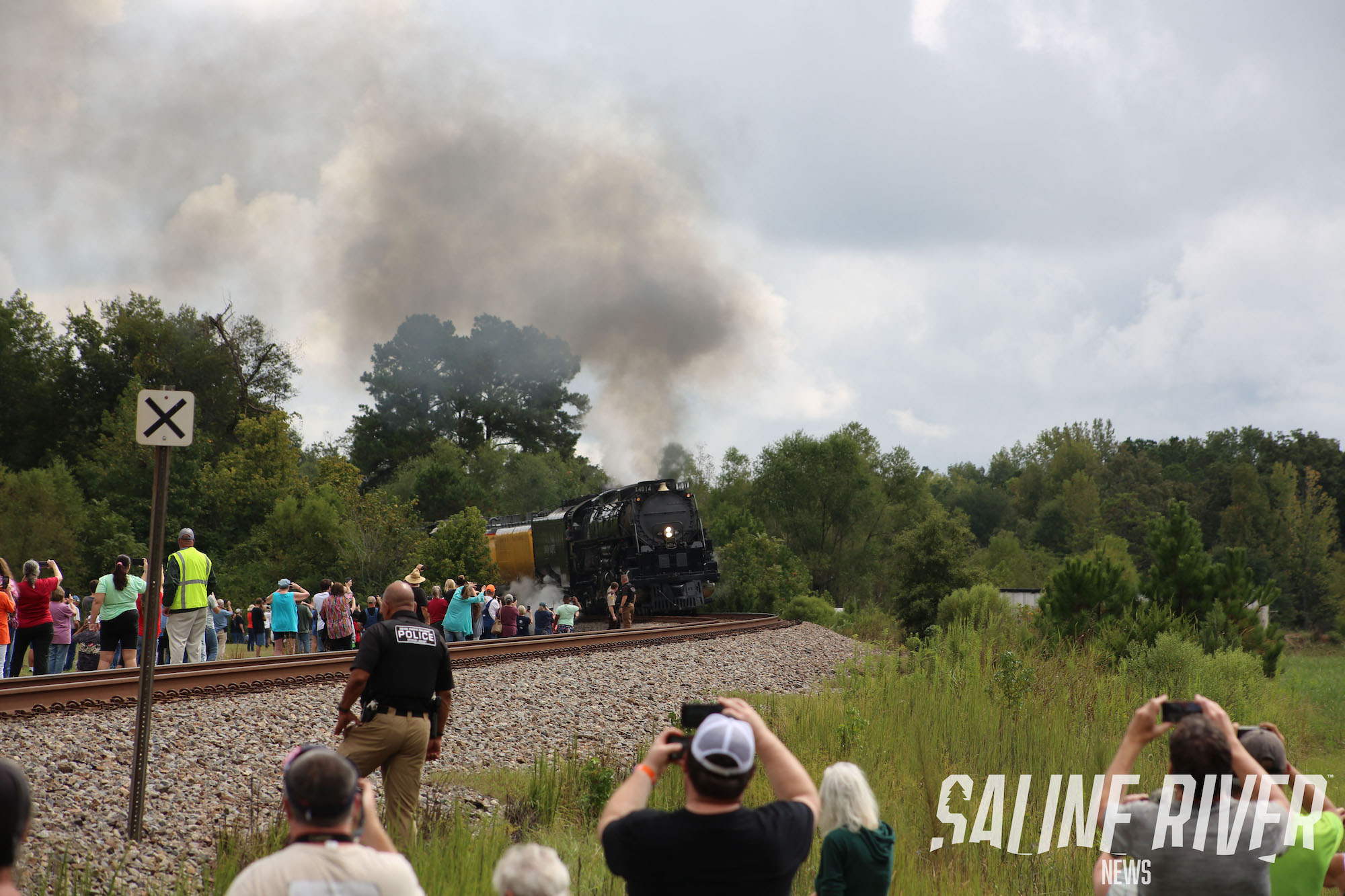 A train is coming down the tracks with people watching.