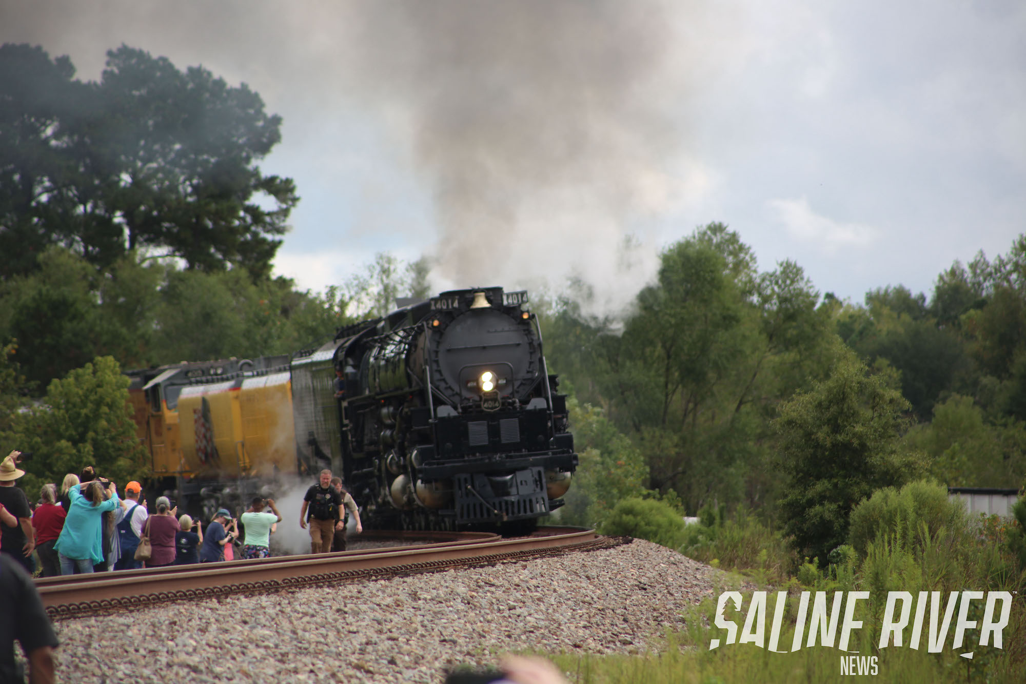 A train is coming down the tracks with people around.