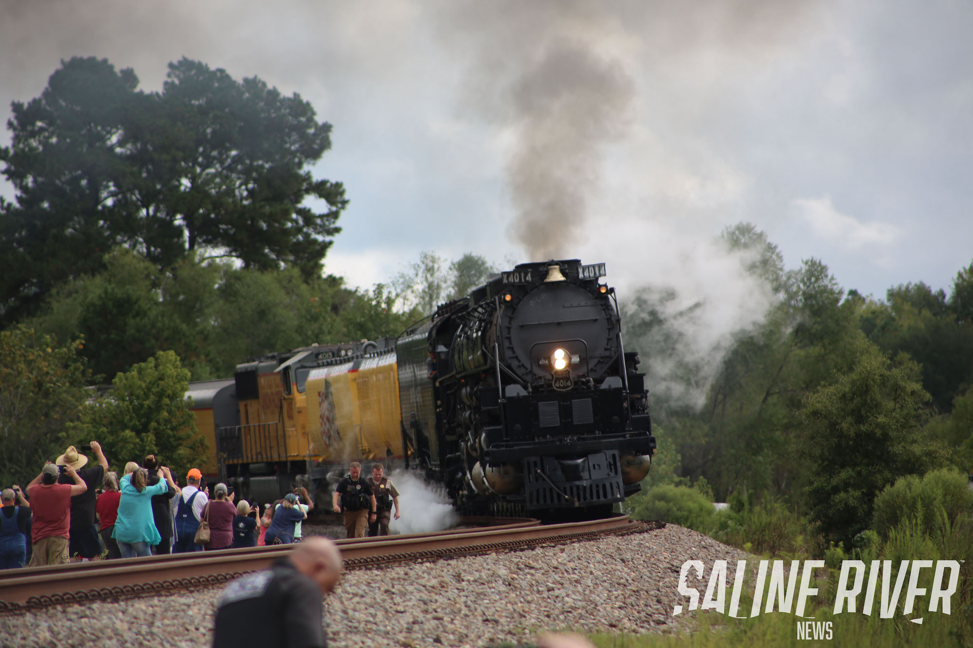 A train is coming down the tracks with people watching.
