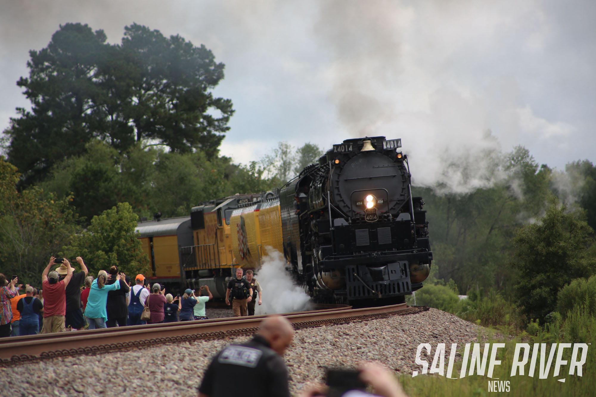 A train is coming down the tracks with people watching.