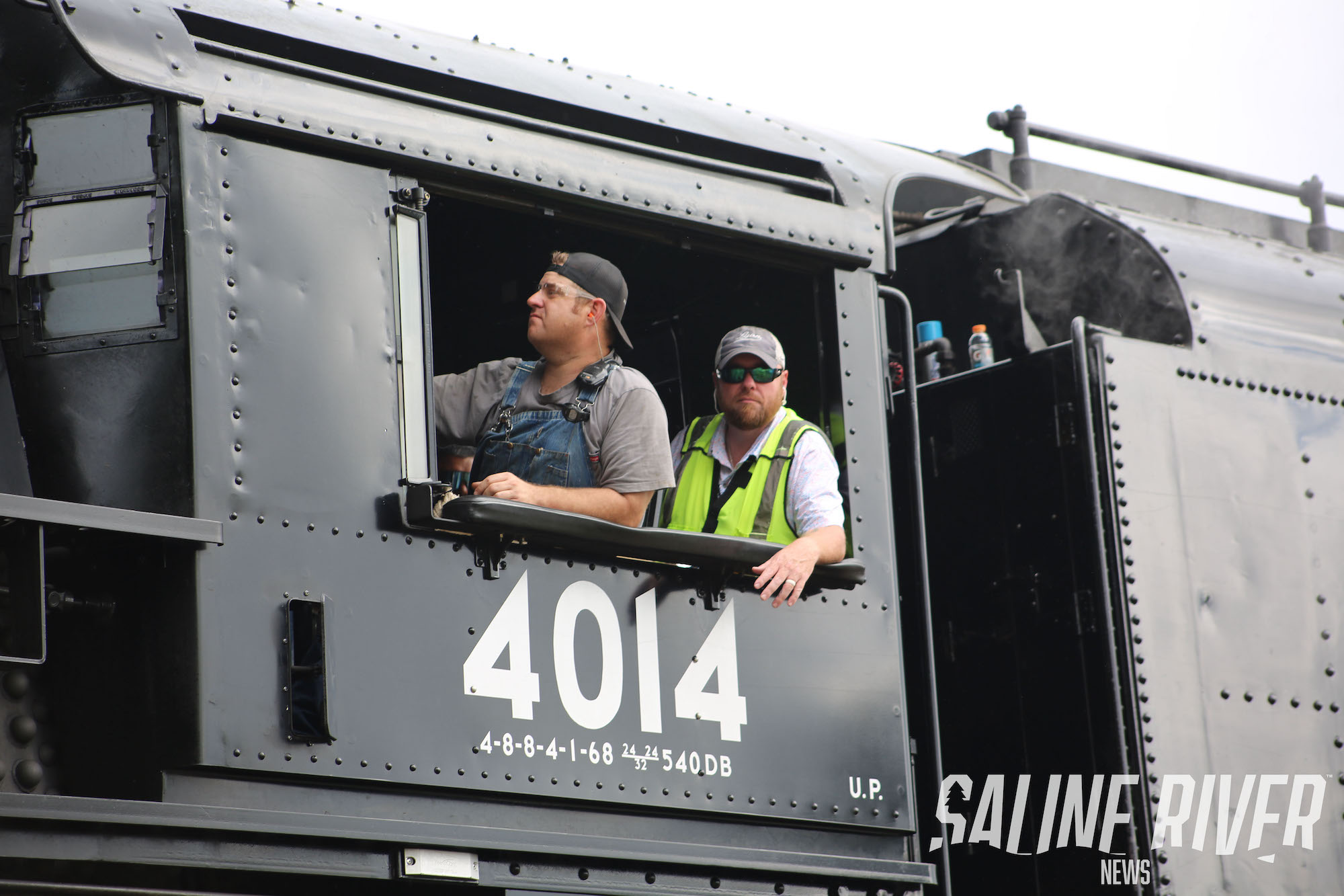 Two men in a train car looking out the window.