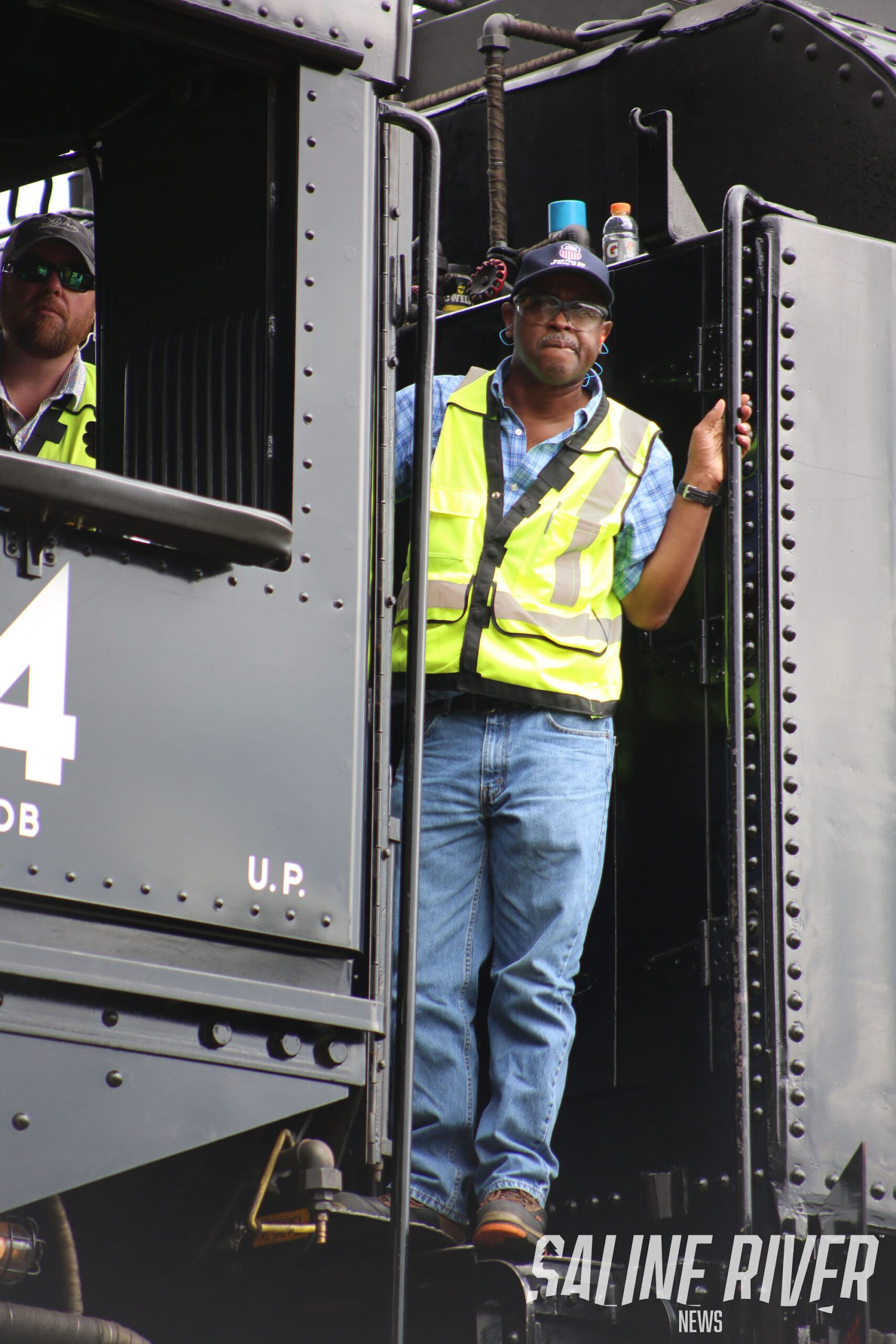 A man in safety vest standing on the side of train.