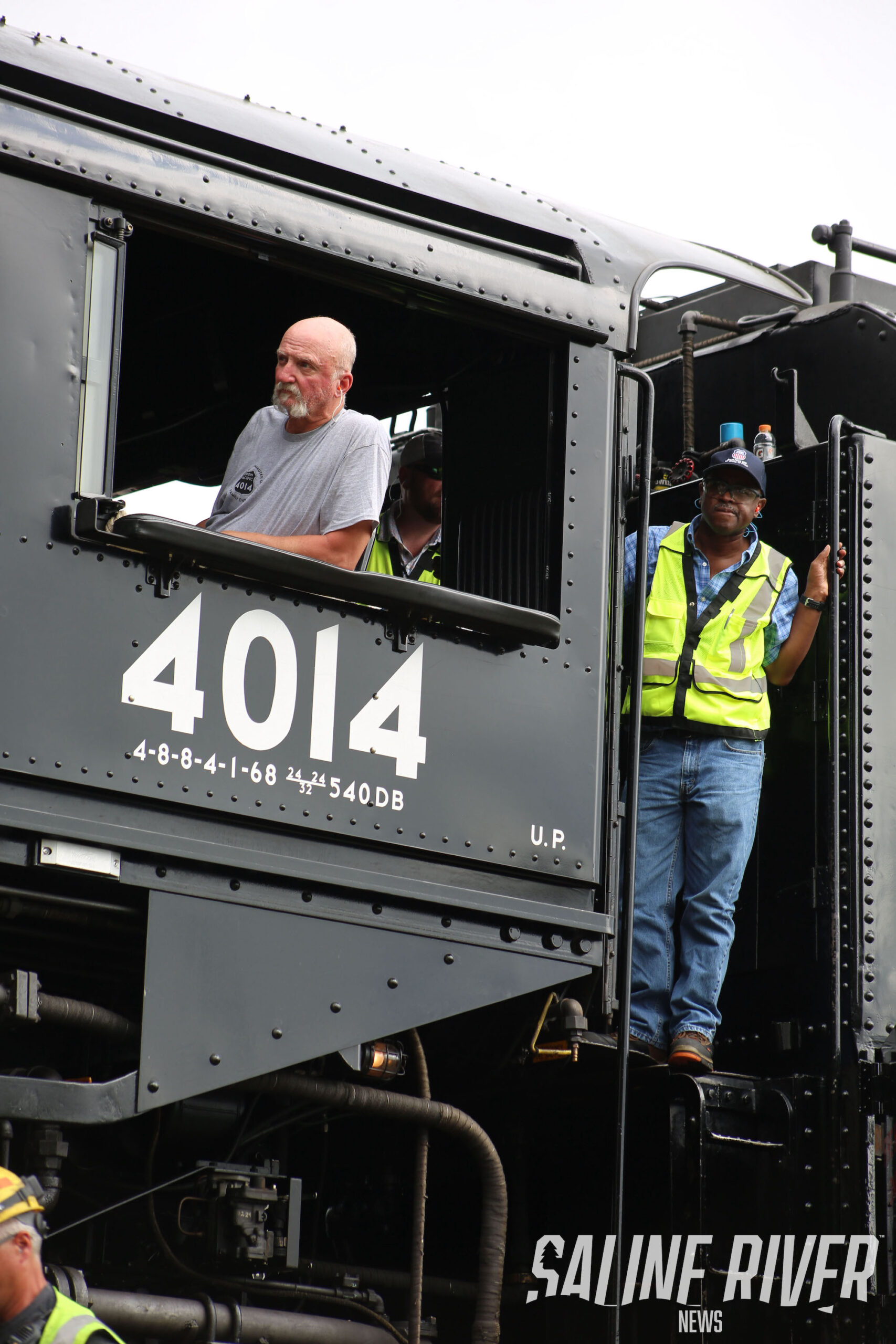 A train conductor and two men in the window of an old locomotive.