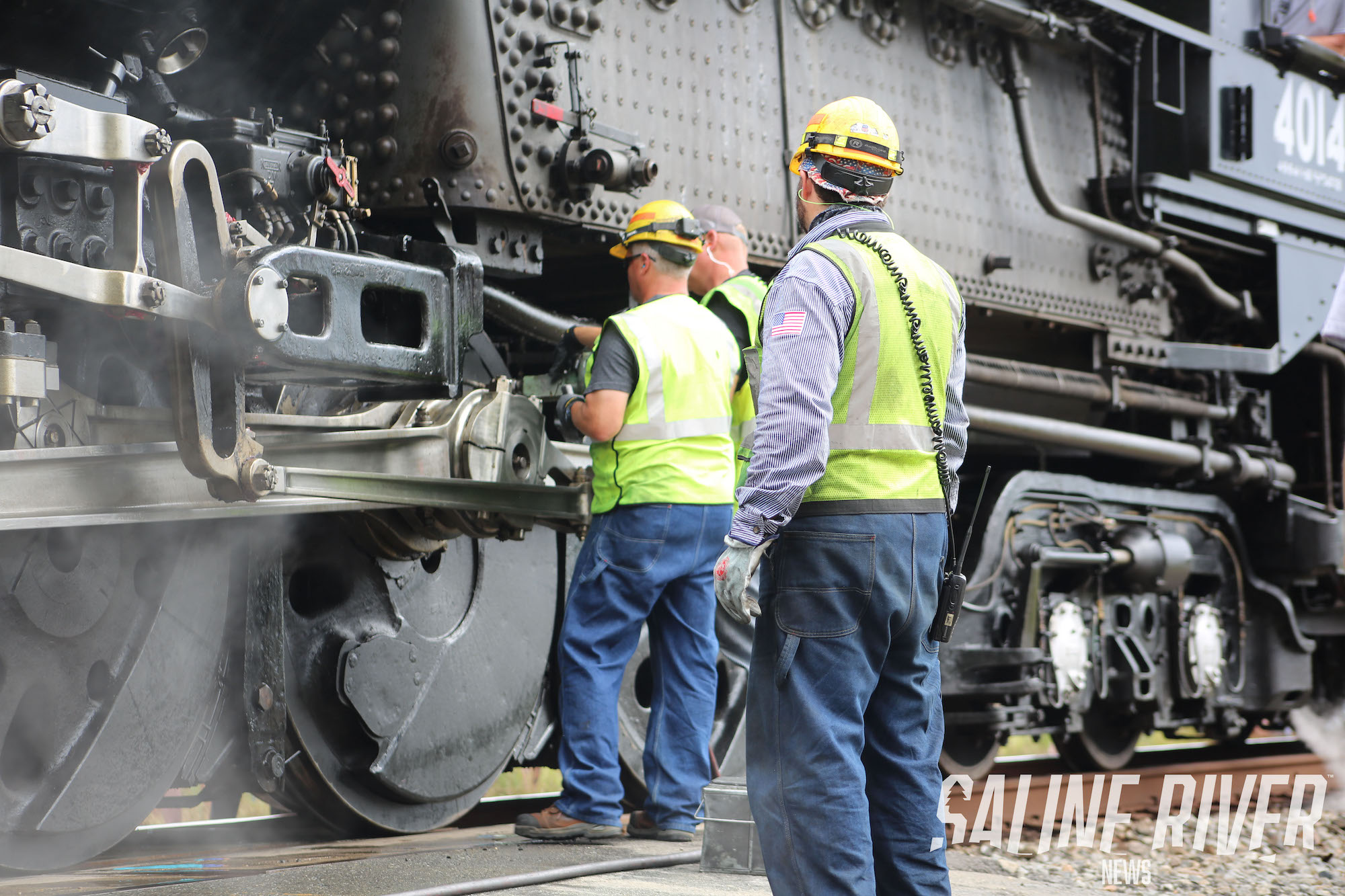 Two men in safety vests and hard hats working on a train.