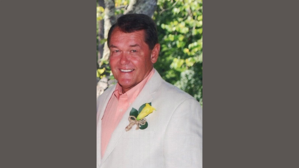 A man in a white suit and pink shirt.