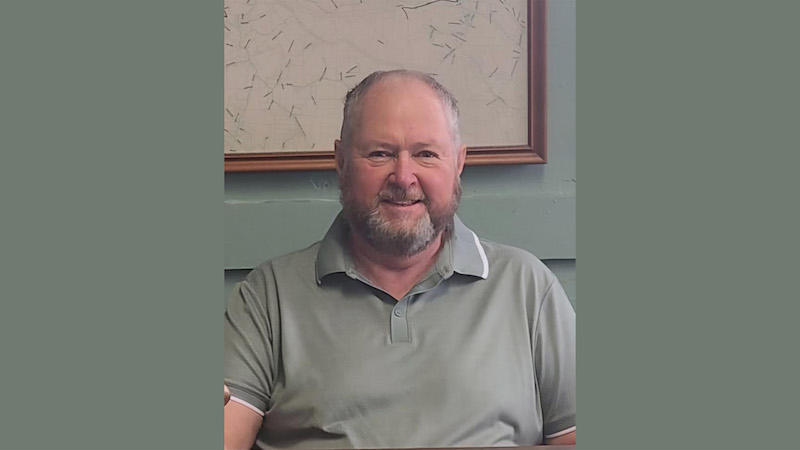 A man with a beard and mustache sitting in front of a wall.