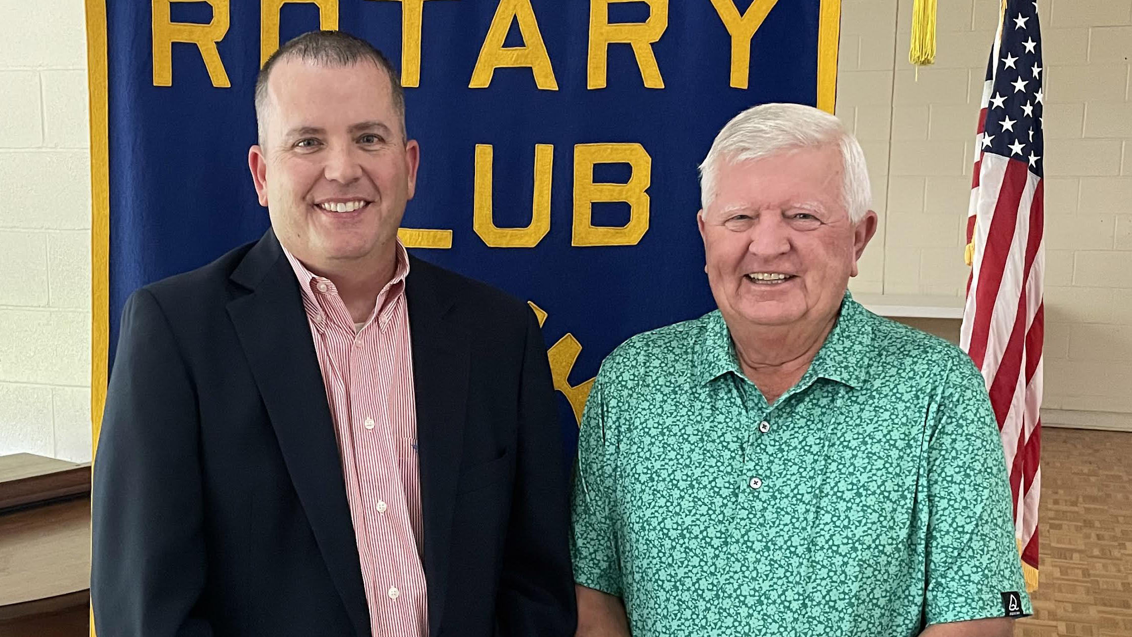 Two men standing next to each other in front of a rotary club sign.