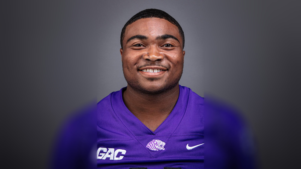 A man in purple football uniform smiling for the camera.