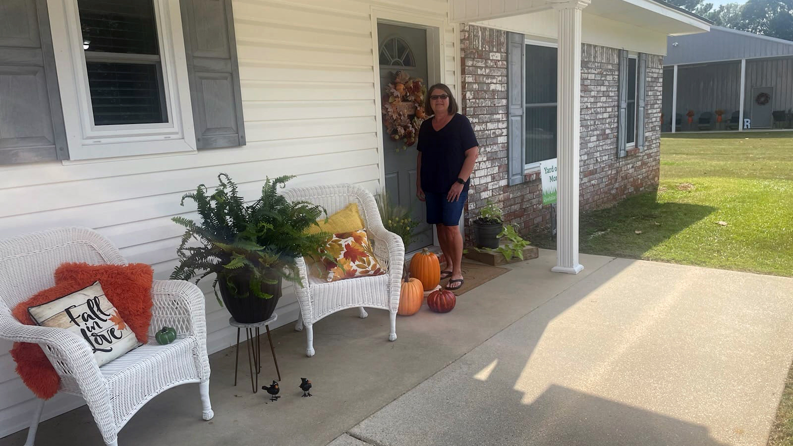 A woman standing in front of a porch with white furniture.