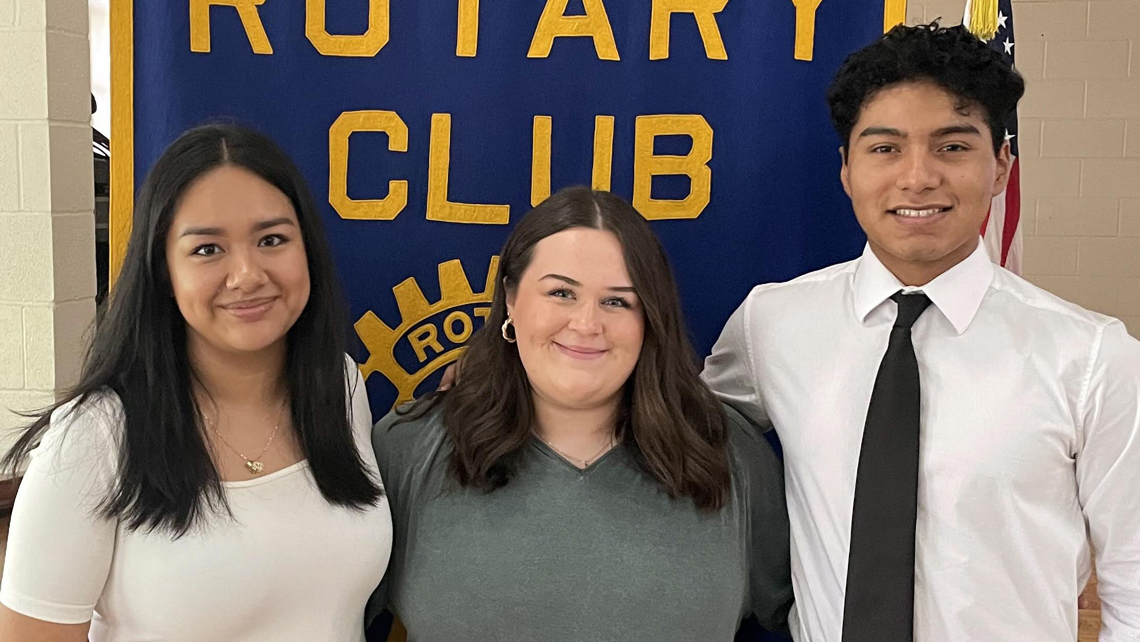 Three people standing in front of a rotary club banner.