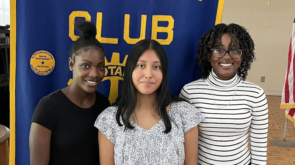 Three young women posing for a picture in front of a banner.