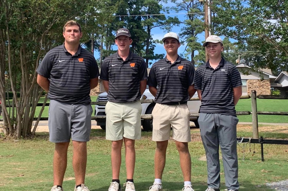 Four men standing on a golf course in their uniforms.