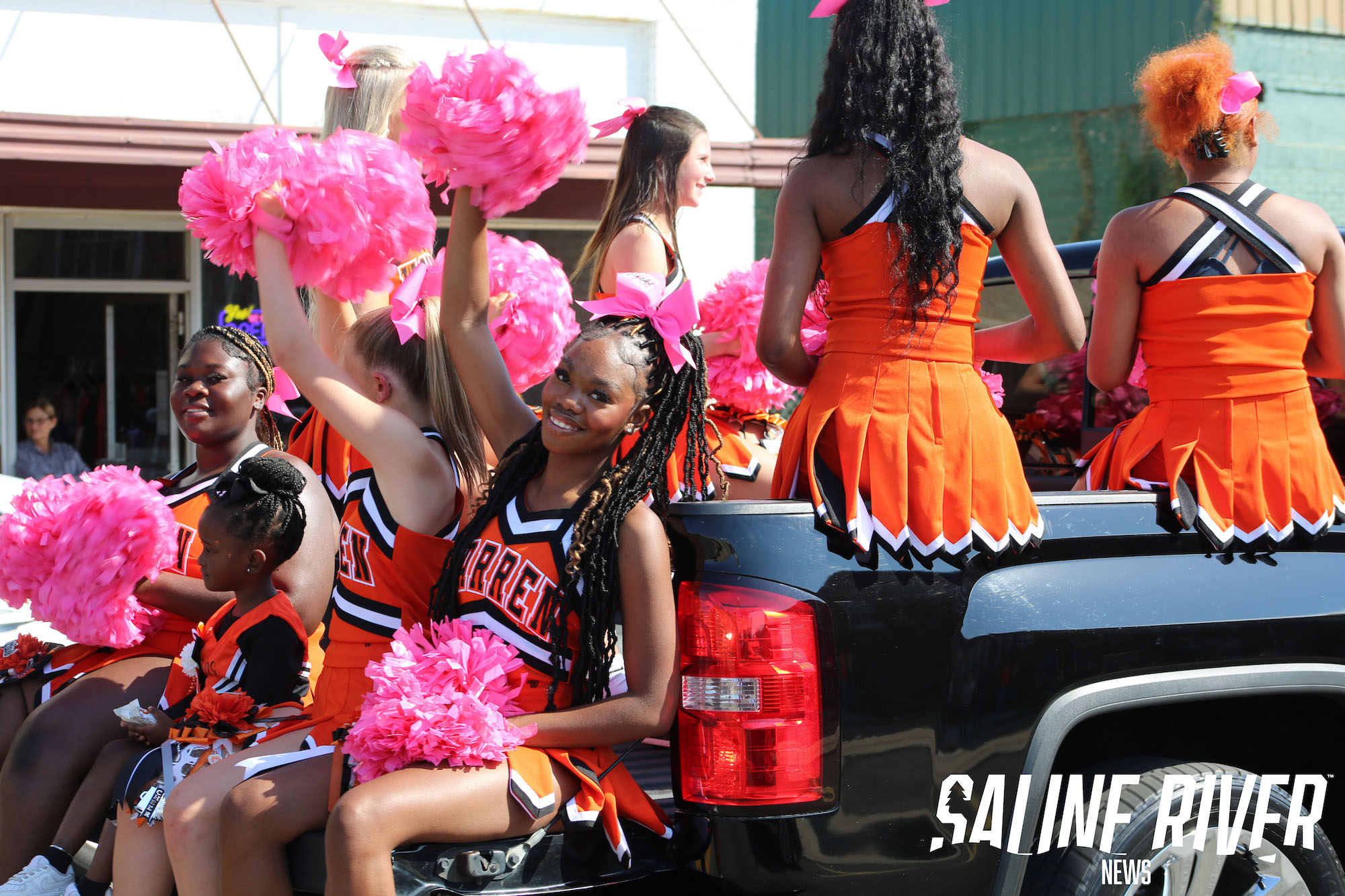 A group of cheerleaders sitting in the back of a truck.