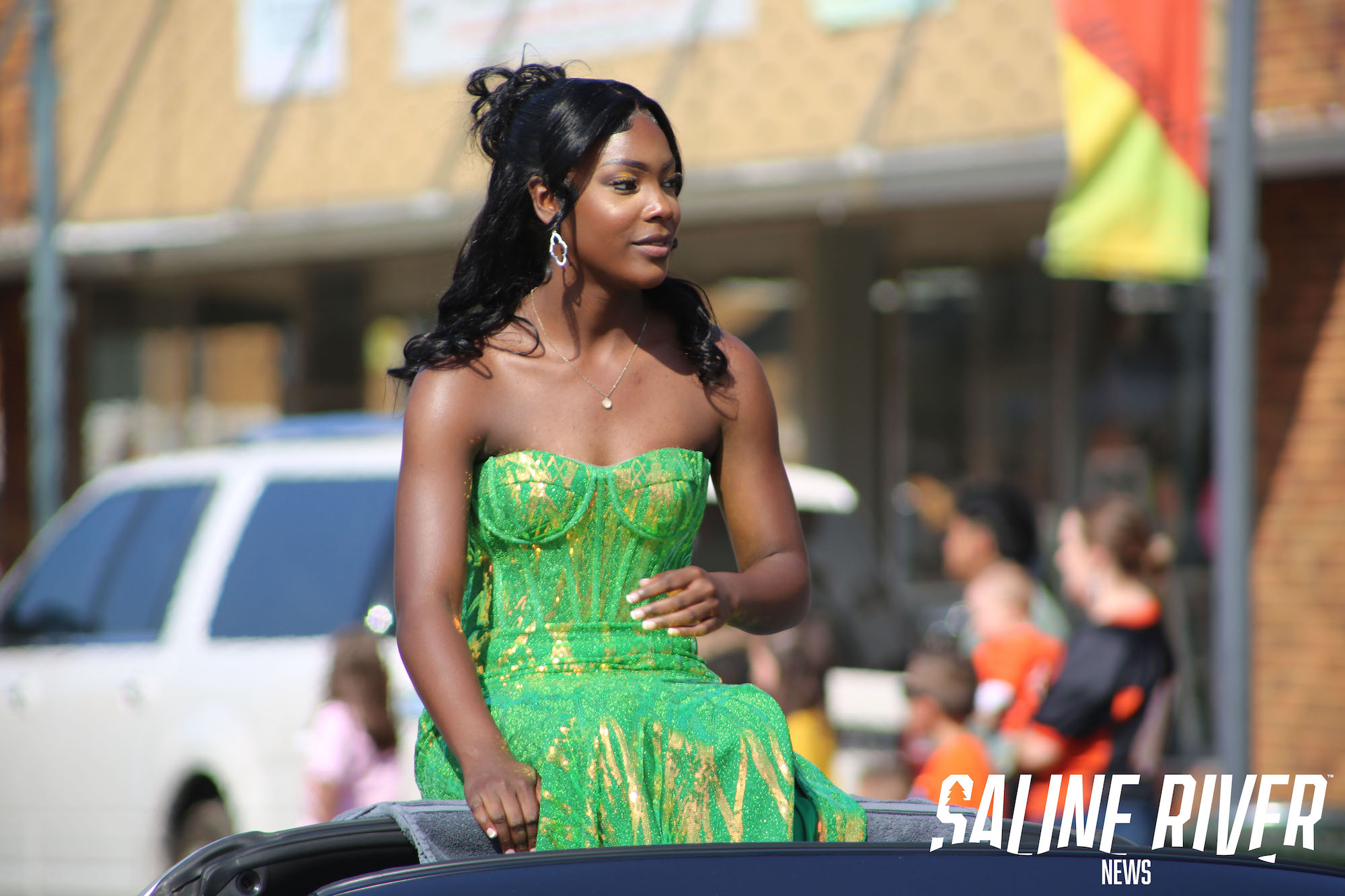 A woman in green dress sitting on top of car.