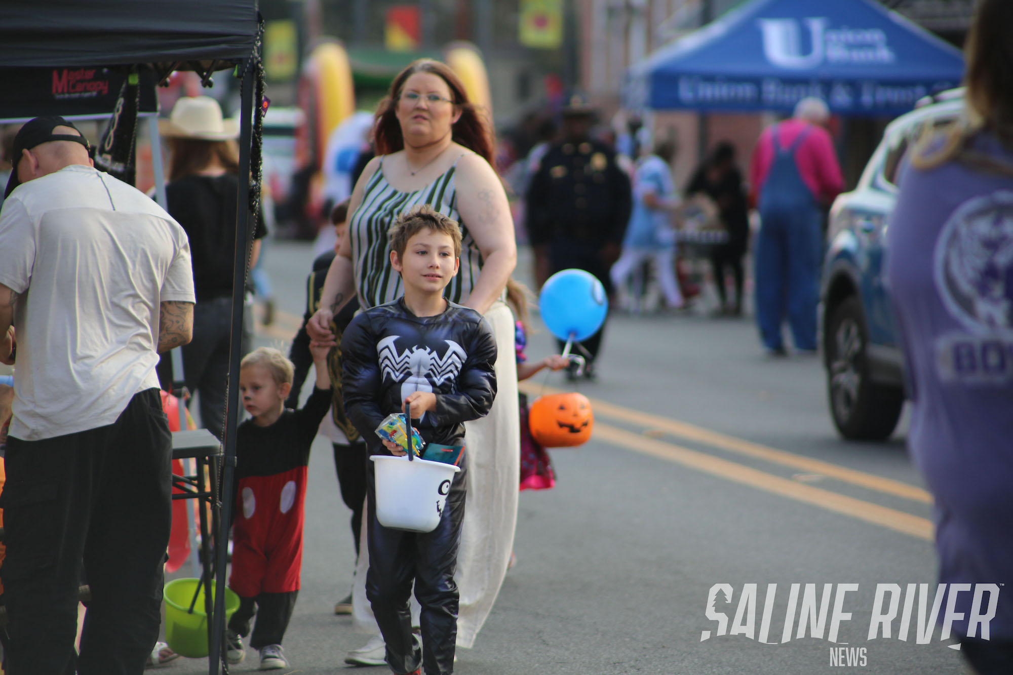 A boy is walking down the street with his mother.