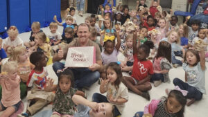 A group of children sitting on the floor with one man holding up a sign.