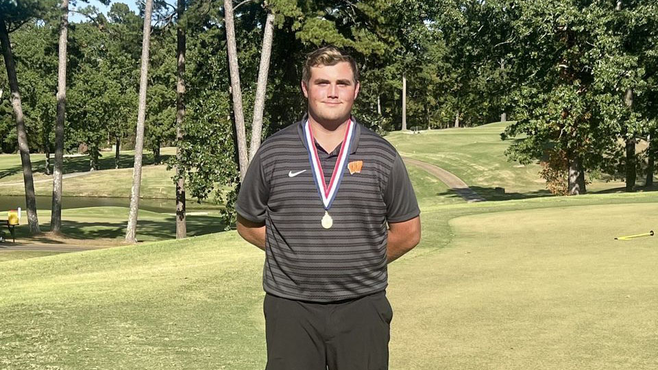 A man standing on top of a golf course holding his medal.