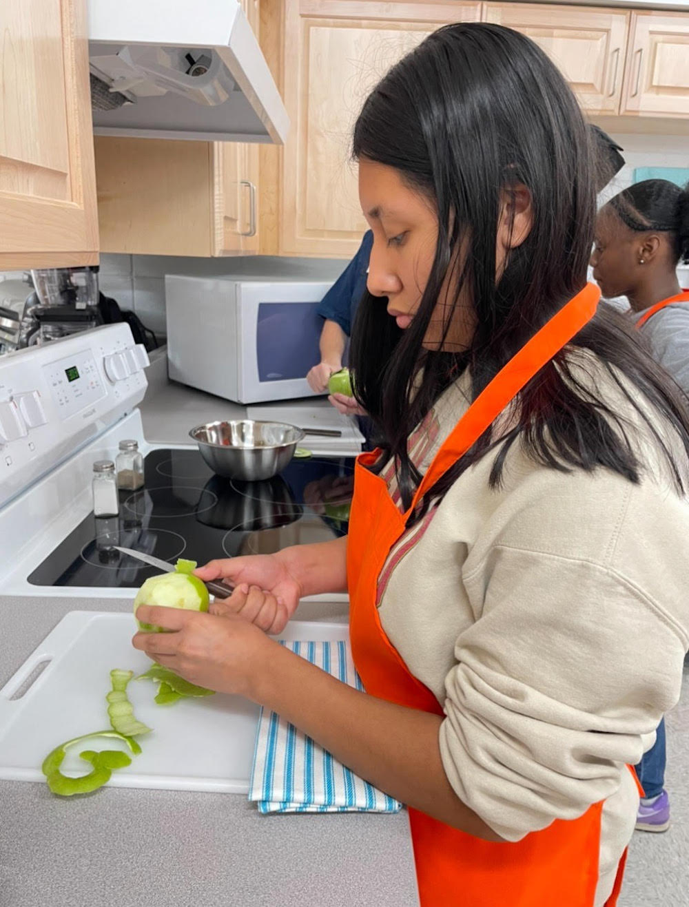 A woman in an orange apron cutting up fruit.