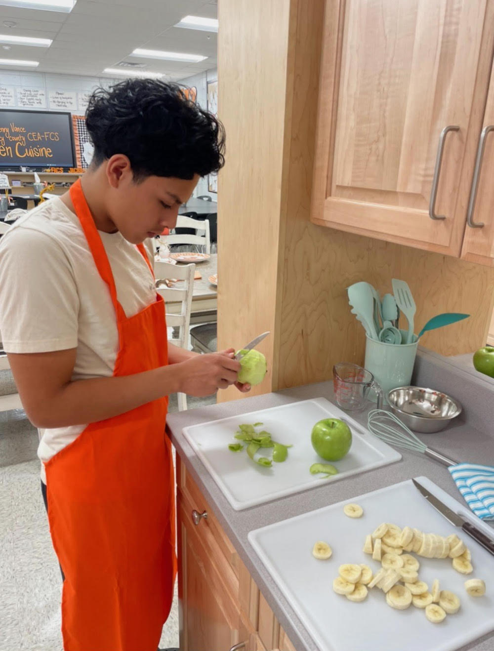 A person in an orange apron cutting apples.
