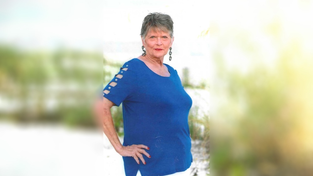A woman standing in front of bushes and trees.
