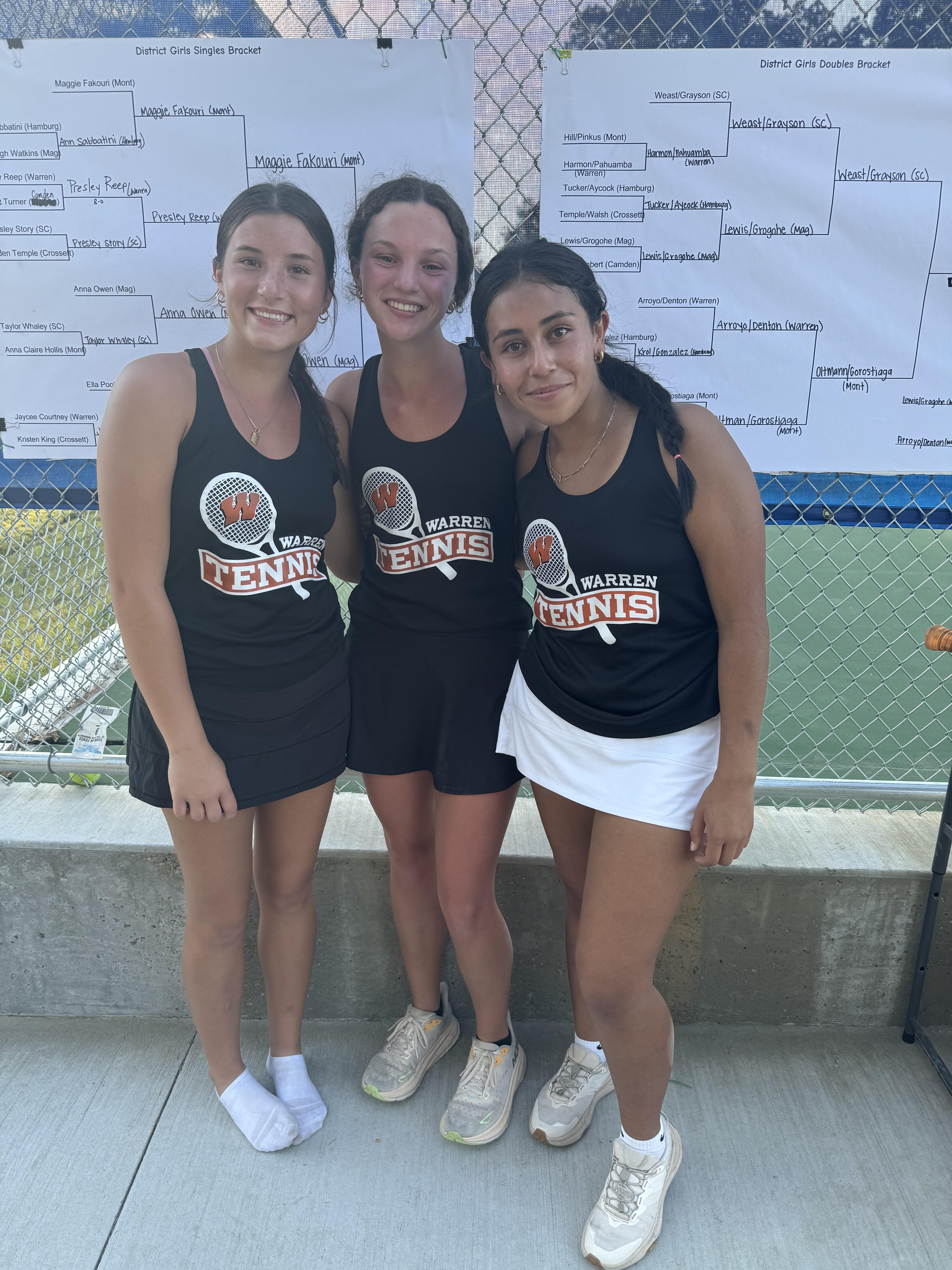 Three girls are posing for a picture on the tennis court.