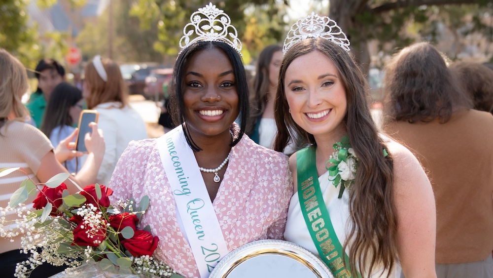 Two women are posing for a picture while holding flowers.