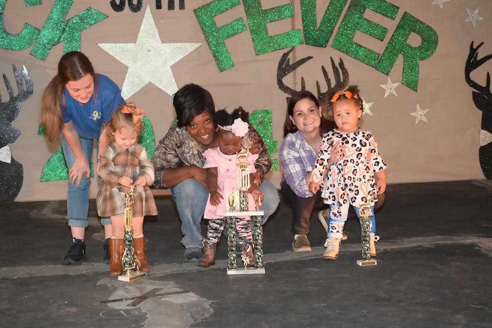 A group of people standing on the stage with some little girls.