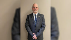 A man in a suit and tie standing with his hands crossed.