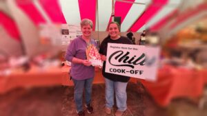 Two women holding a sign that says " my sister sure for the chili cook-off ".