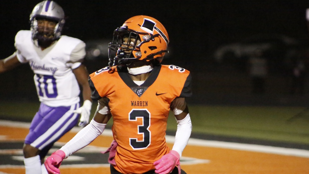 A football player in an orange uniform is walking on the field.