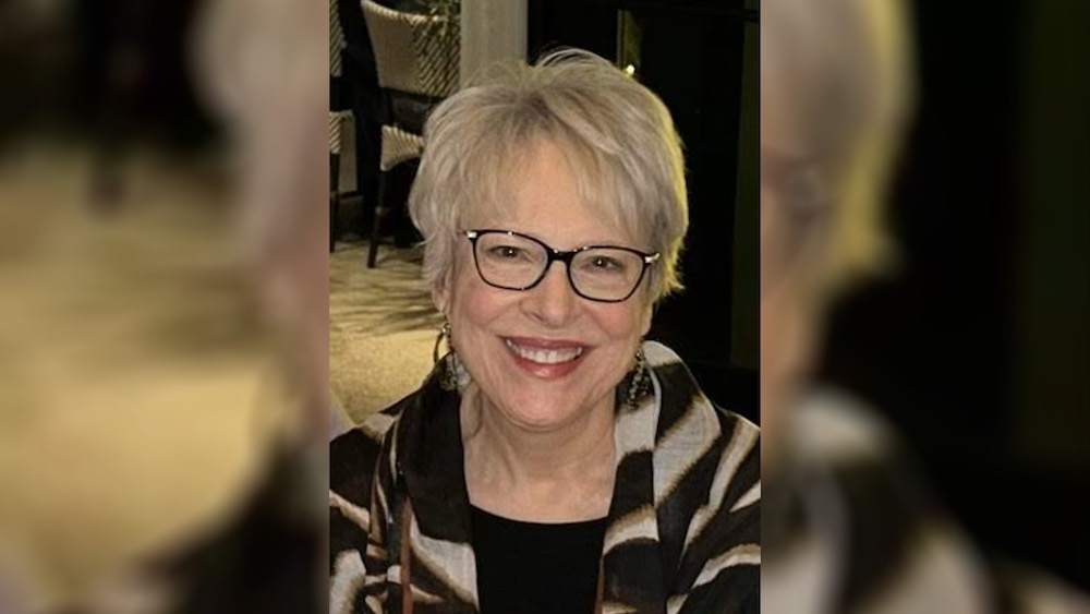 A woman with glasses and white hair smiling.