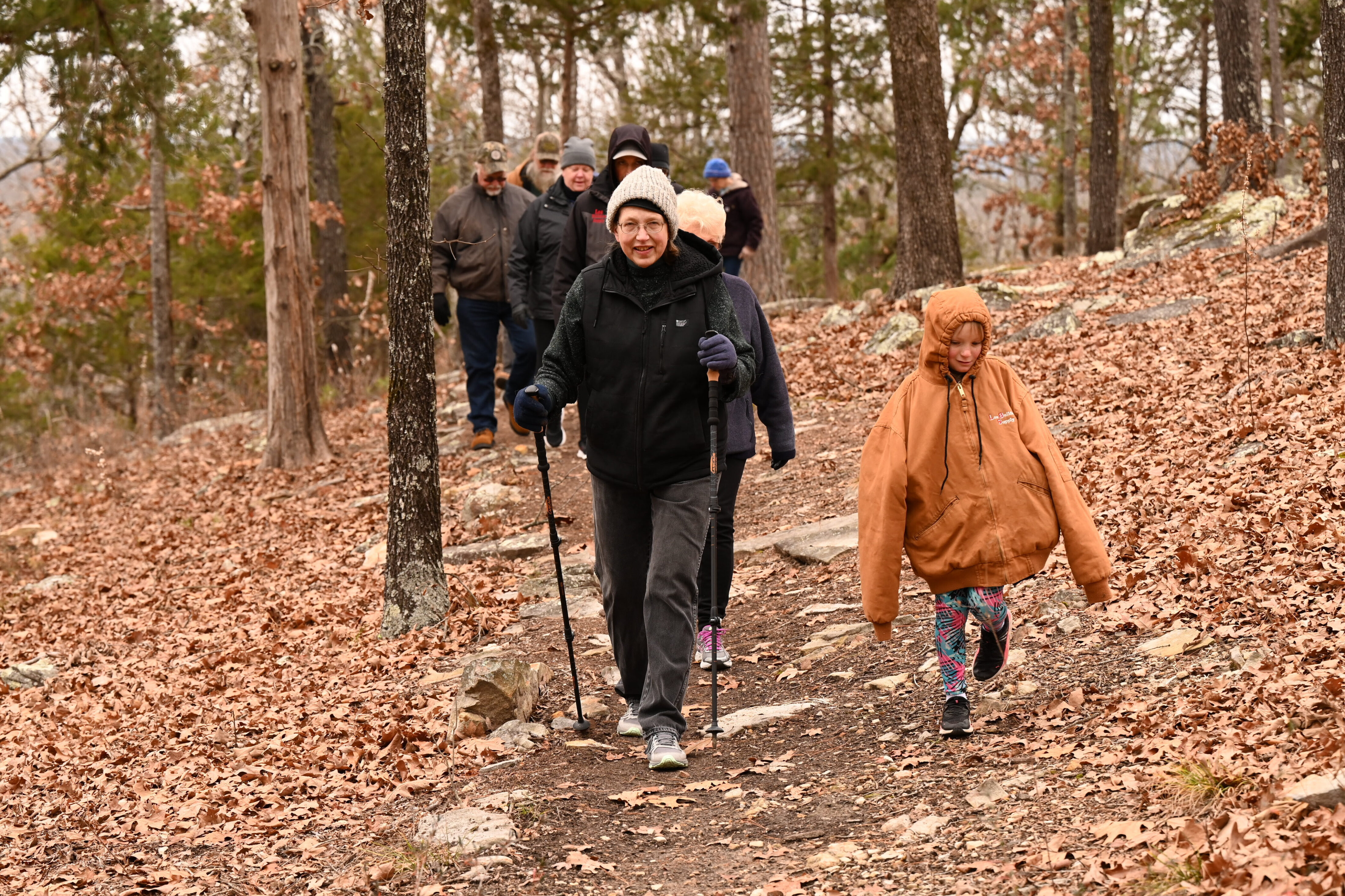 A group of people walking on the trail in the woods.