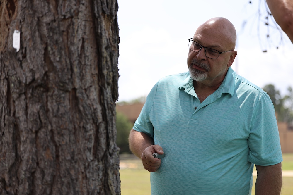 A man in glasses is standing next to a tree