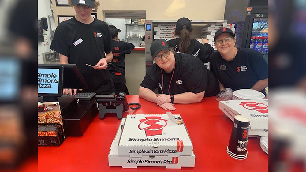 A group of people standing around a table with pizza.