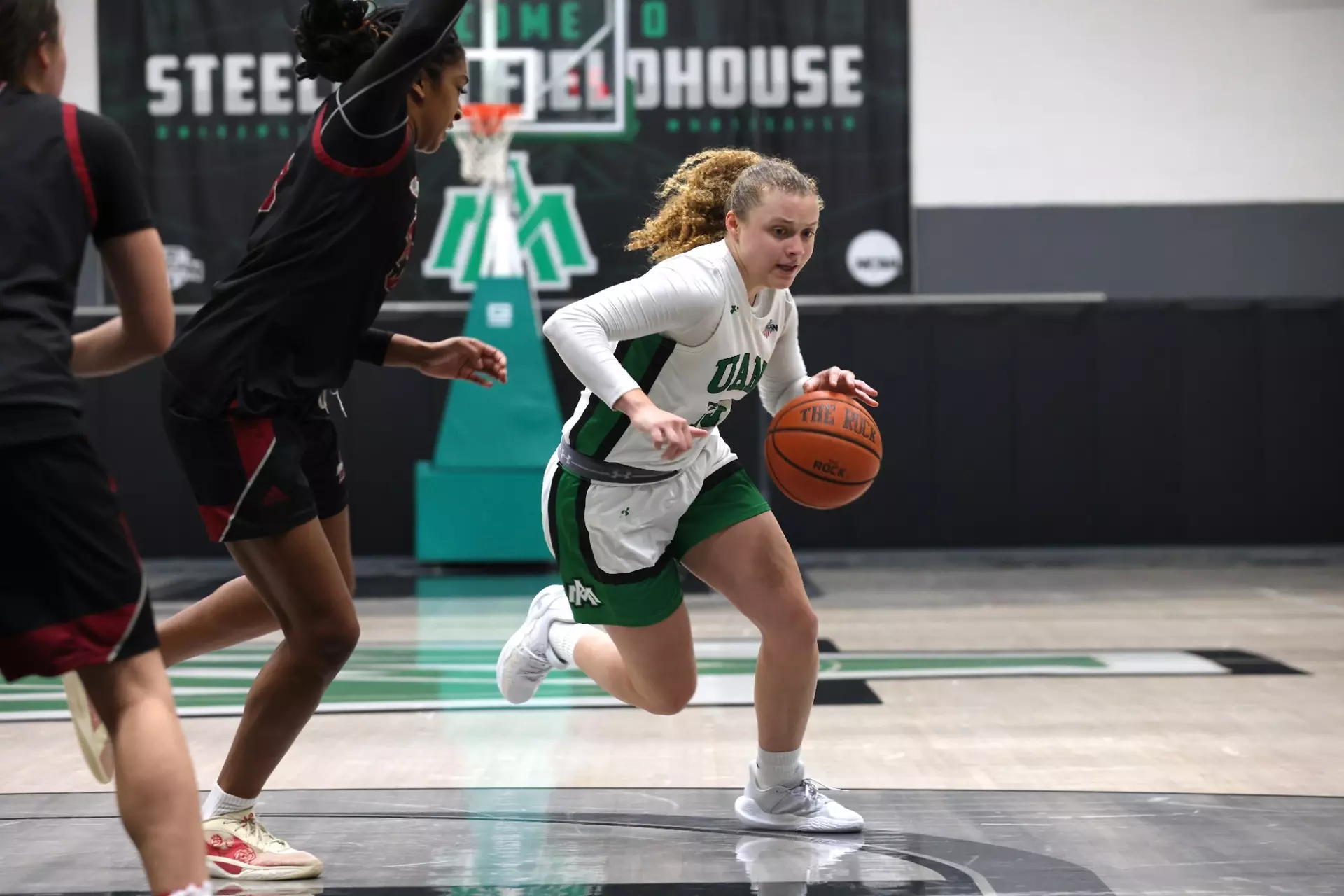 A girl in white and green playing basketball.