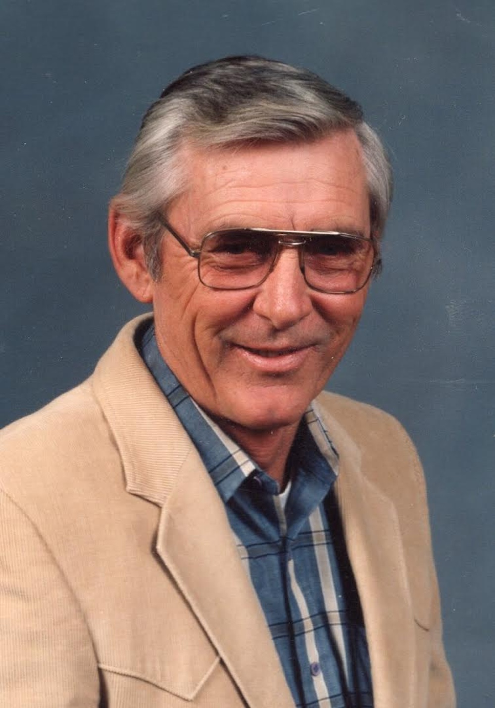 A man in glasses and a jacket is smiling.