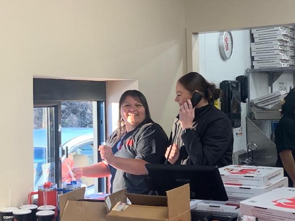 Two women are standing in a room talking on cellphones.