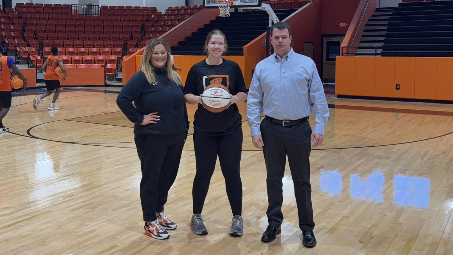 Three people standing in a gym holding a basketball.