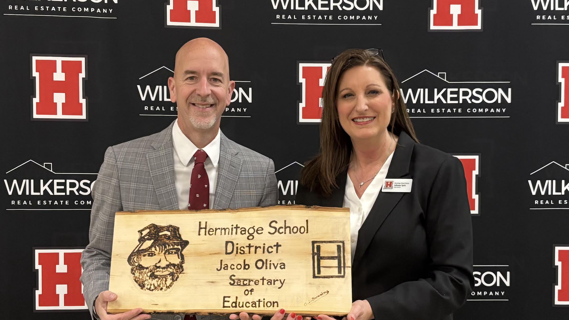A man and woman holding a sign that says " heritage school district, jacob olive supervisory education ".
