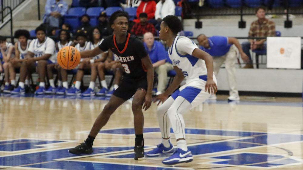 Two men playing basketball on a court with people watching.
